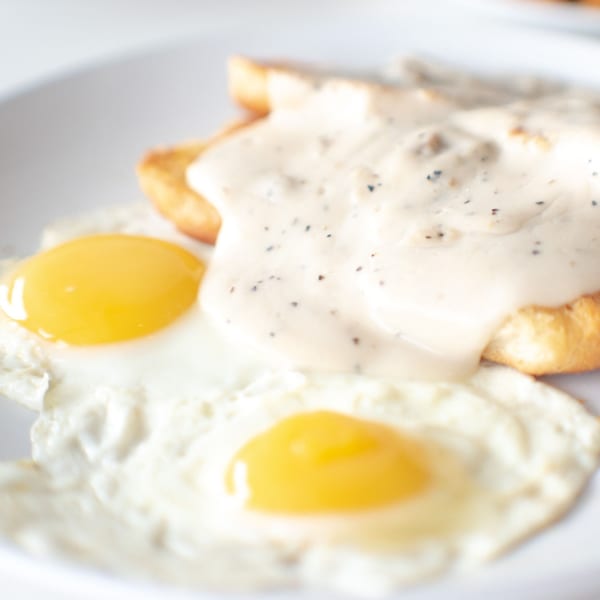 Two fried eggs with runny yolks next to biscuits covered in creamy sausage gravy.