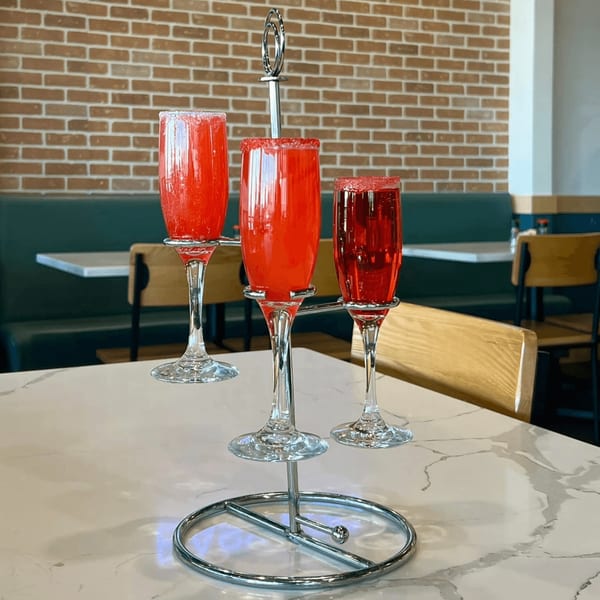 Three red mimosas with sugared rims on a chrome stand, on a white marble table.