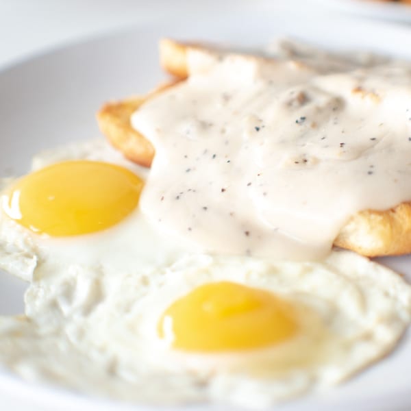 Two sunny-side-up eggs and biscuits with gravy on a white plate at The Easy Egg.