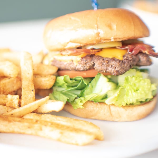 A bacon cheeseburger with lettuce, tomato, and a side of golden french fries on a white plate.