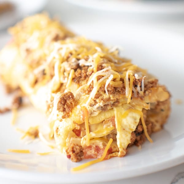 Close-up of a breakfast burrito or enchilada, topped with melted cheese and ground sausage.