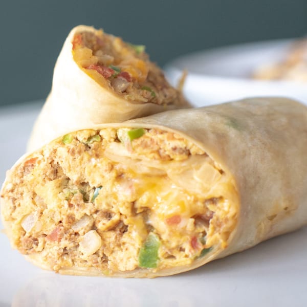 Two breakfast burritos, one cut in half, revealing scrambled eggs, cheese, and vegetables.