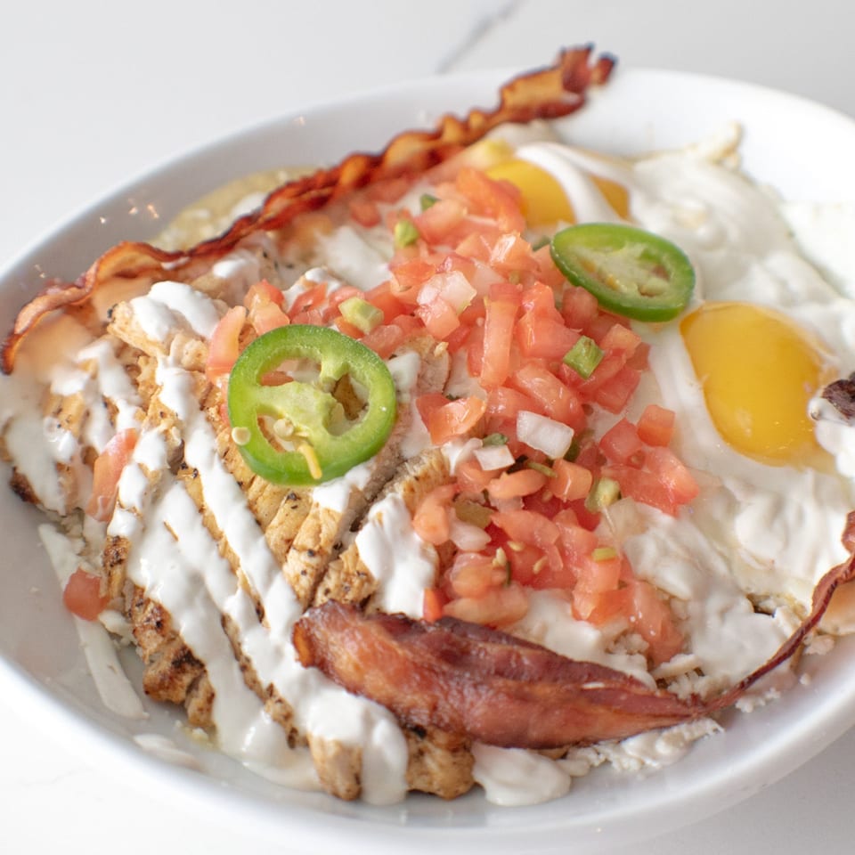 Breakfast bowl with chicken, bacon, fried eggs, pico de gallo, jalapeños, and white sauce.