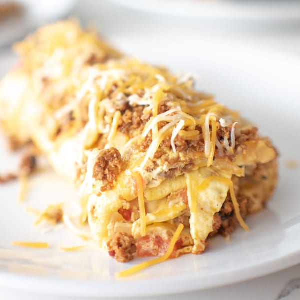 Close-up of a breakfast burrito or enchilada, topped with melted cheese and ground meat.