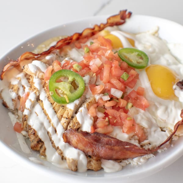 Breakfast bowl with chicken, bacon, fried eggs, pico de gallo, jalapeños, and white sauce.