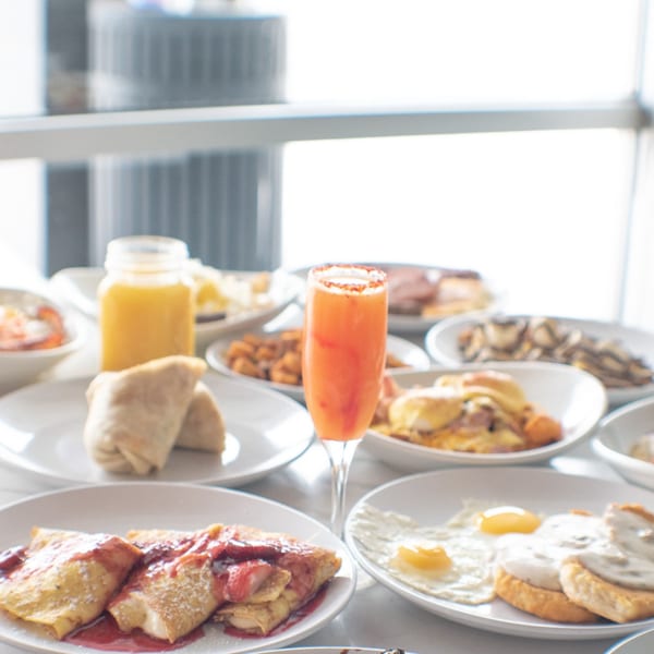 A table laden with various breakfast dishes, including crepes, eggs, and a mimosa.